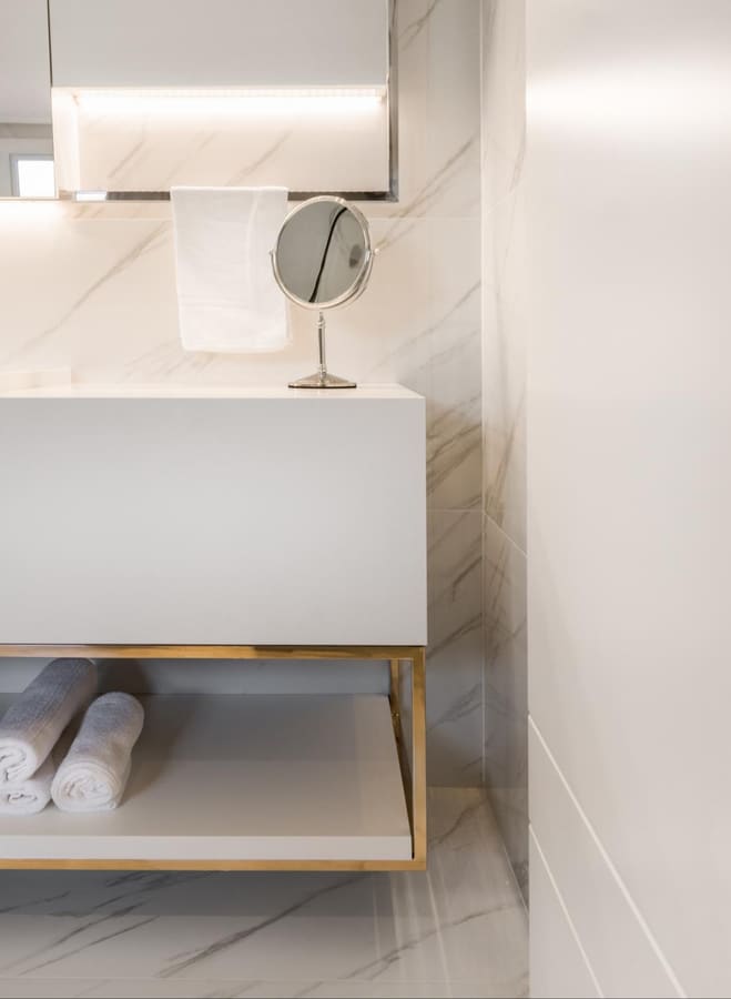Marble bathroom vanity with a brass-framed open shelf for towels