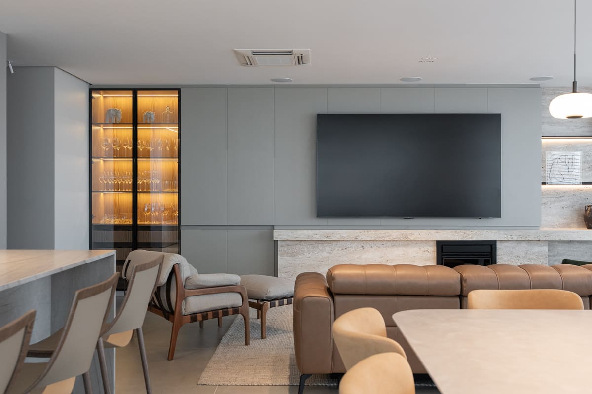 Open living and dining room with a grey media wall, a lit glass-front bar cabinet and a stone fireplace
