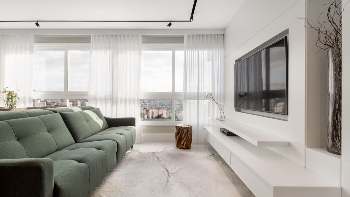 Bright living room with a green sofa, sheer curtains and a floating media unit