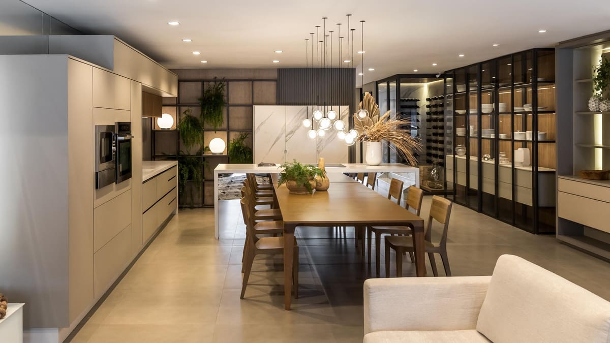 Open kitchen with a long wood dining table, pendant lights and a glass-fronted wine and display wall