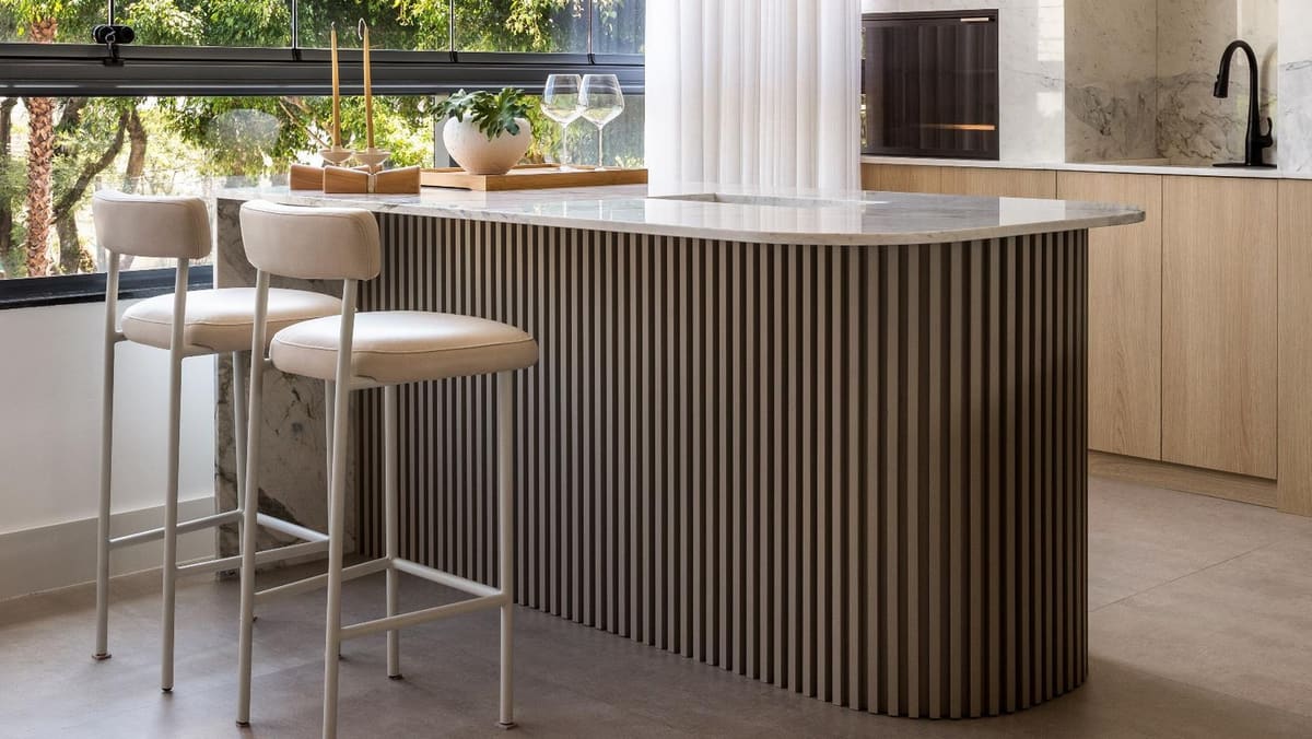 Kitchen island with a curved fluted base and a stone top beside an open window