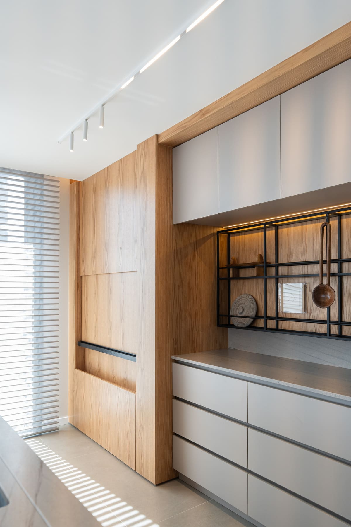 Wood and grey kitchen wall with a black metal utensil rail and handleless drawers