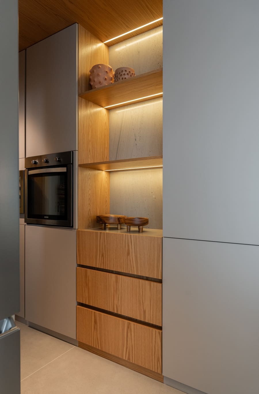 Tall oven column with lit wood shelves and wood-front drawers