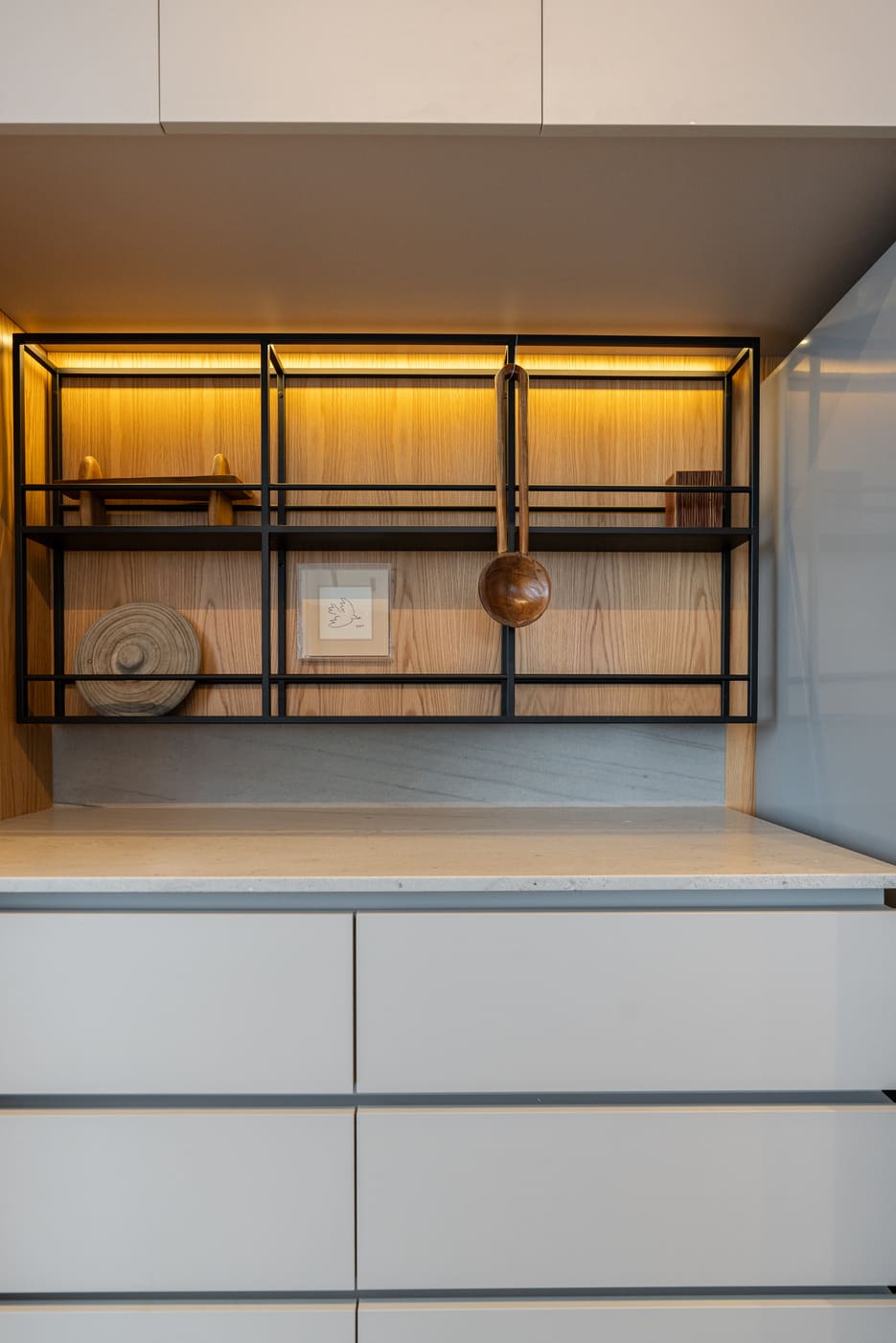 Lit black metal shelving above grey handleless drawers