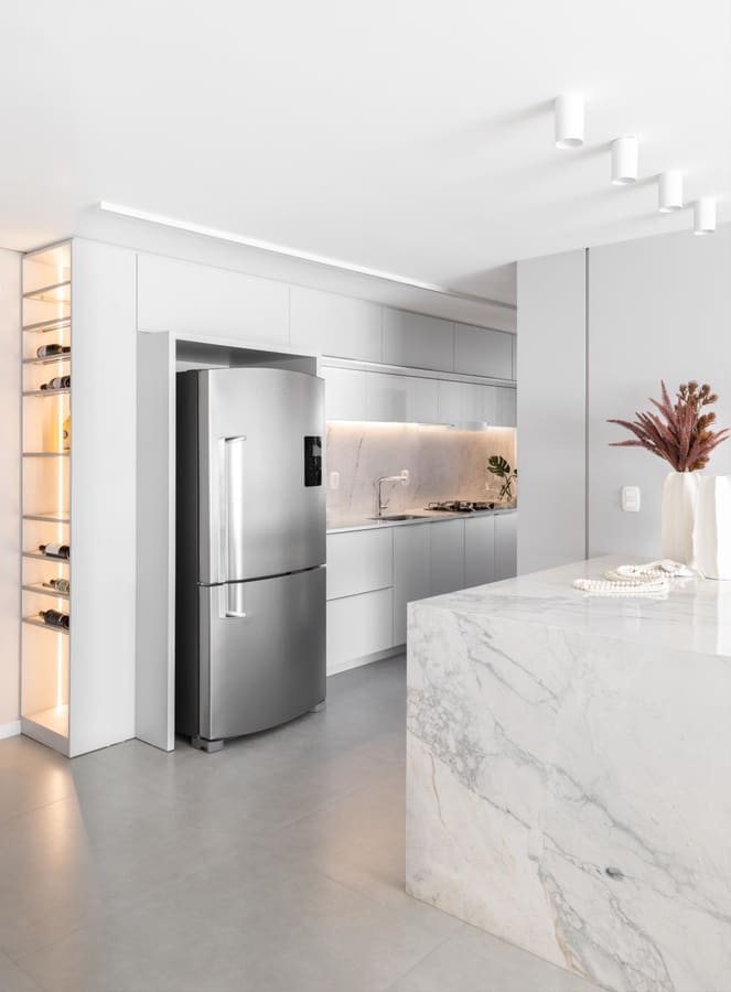 White kitchen with a marble waterfall island and a lit wine niche