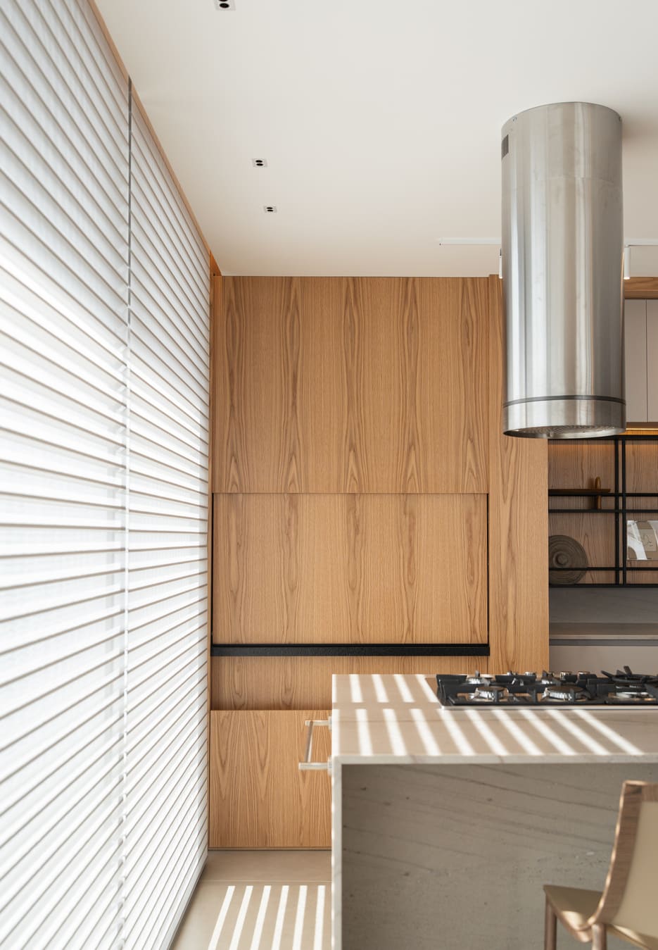 Wood-paneled kitchen wall with a cylindrical stainless hood over a cooktop island