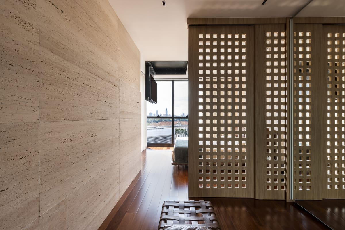 Travertine wall and perforated wood screen doors along a bedroom corridor